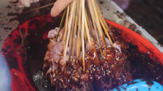 Close-up footage of traditional Filipino street food known as Isaw, featuring marinated and skewered chicken or pig intestines being dipped into a rich, dark savory-sweet barbecue sauce. This popular 