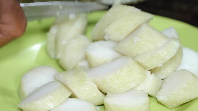 A close-up shot showing the process of slicing lontong, a traditional Indonesian compressed rice cake wrapped in banana leaves. The white, dense rice cakes are cut into bite-sized pieces and served on