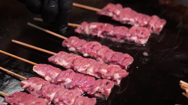 Close-up shot of fresh raw meat pieces, such as beef, mutton, or goat, expertly threaded onto traditional thin wooden skewers. The footage showcases the marination and preparation phase of authentic A