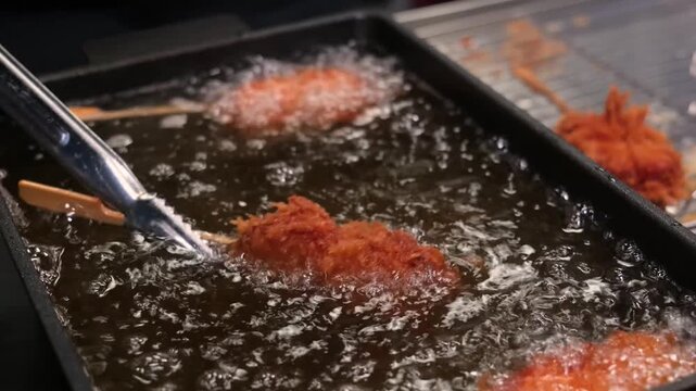Close-up footage of traditional Korean corn dogs being deep-fried in a vat of bubbling hot oil until golden brown. The skewers are coated in a thick, textured batter and panko breadcrumbs, showcasing 