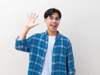 Happy young Asian man with glasses waving his hand while greeting against an isolated white background © Muhammad Alimaki