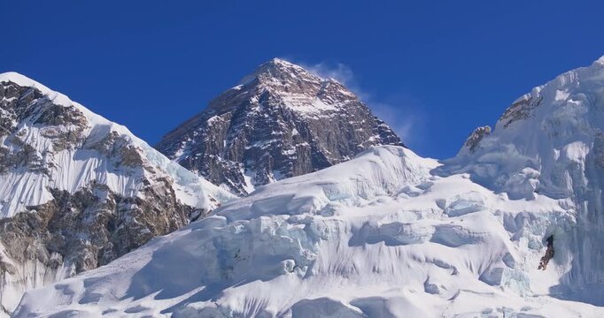 Everest region, Nepal, drone aerial sideways glide shot capturing the dark rocky peak of Mount Everest with a blowing snow plume at the summit rising behind the snow-capped slopes of Nuptse.