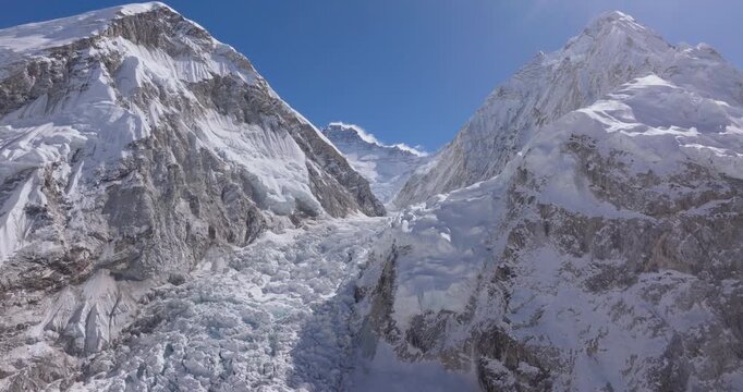Khumbu Icefall, Everest, Nepal, drone aerial slow glide shot over the fractured ice formations, seracs, and crevasses of the icefall valley, framed by steep mountain slopes under a clear blue sky