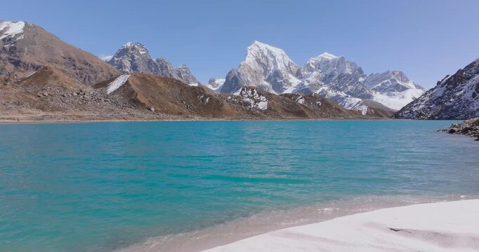 Gokyo Lake, Khumbu Everest Region Nepal drone aerial panoramic orbit shot rotating around the turquoise waters of blue glacier lake, with Cholatse and Taboche himalayas in the distant background