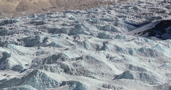 Khumbu Icefall, Everest, Nepal, overhead drone aerial glide-in shot moving closer to fractured glacial ice structures, deep crevasses, and rugged snow-covered textures.