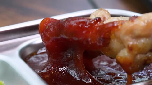 A macro, slow-motion shot showing a piece of tender, golden-brown roasted pork knuckle being dipped into a smooth, savory dark gravy or BBQ sauce. The footage highlights the succulent texture of the m