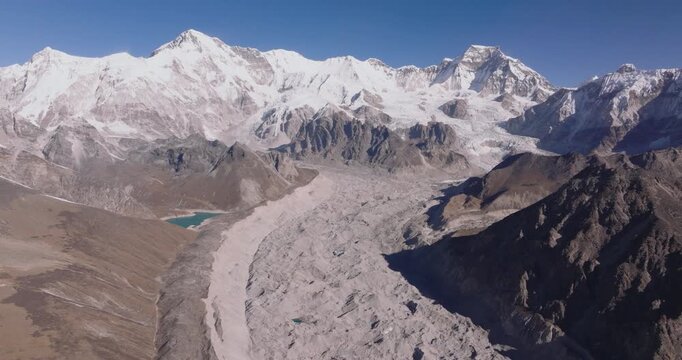 Everest region, Nepal, drone aerial shot of the massive Ngozumpa Glacier winding through a rugged alpine valley beneath the snow-capped peak of Cho Oyu.
