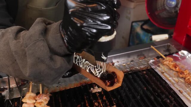 Close-up of a chef in an authentic Japanese izakaya applying a savory-sweet tare sauce to chicken skewers (yakitori) while they are expertly grilled over charcoal. The footage highlights the tradition
