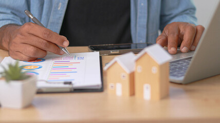 Real estate professional analyzing property market data and investment reports on a laptop. House...