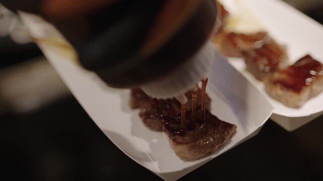 A professional close-up shot of perfectly seared Japanese Wagyu beef cubes. The tender, medium-rare steak is served on a rectangular white plate, showcasing a rich, juicy texture and glistening fat. T