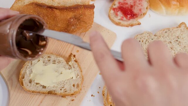 Person Scooping Chocolate Hazelnut Spread from Jar onto Sliced Bread