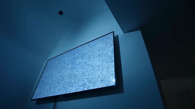 Mid Scene: Blue Wall Mounted Screen Radiates Glow in Dim Room