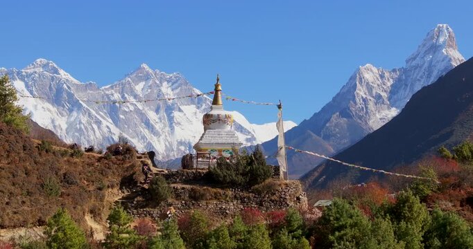 Namche Bazaar, Nepal, drone pull-out shot of a trekker and a local porter carrying a doko basket past a Buddhist stupa with Mount Everest and Mount Lhotse, green hills, and muddy slope in the frame