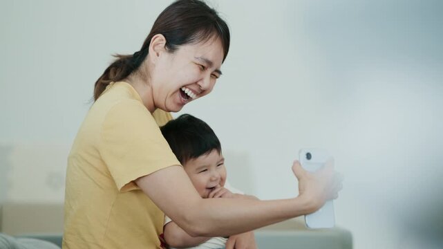 4K Video of a happy Asian mother and her baby boy taking a selfie on a smartphone at home.