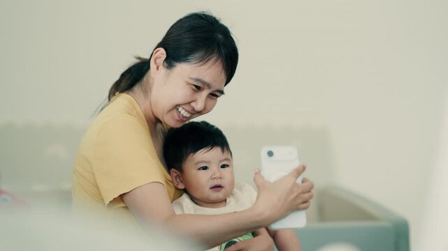 4K Video of a happy Asian mother and her baby boy taking a selfie on a smartphone at home.