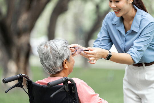 Asian Daughter Helping Senior Mother with Eyeglasses in Wheelchair at Park