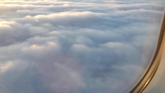 Midflight sunrise ascent above clouds through cabin window