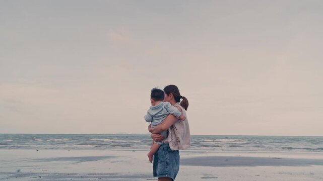 4K Video of an Asian mother holding her baby boy and looking at the sea view on the beach.