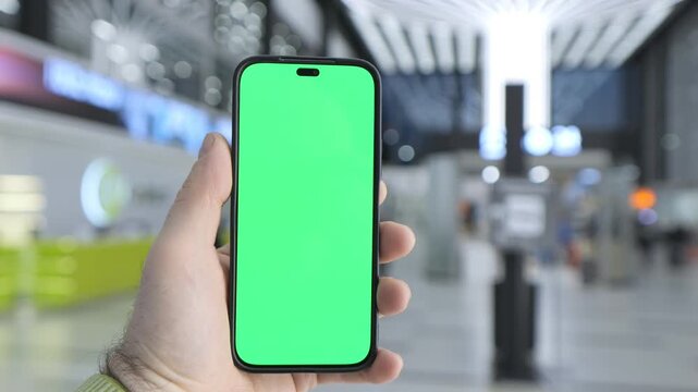 Hand holds smartphone with green screen. Background is blurred train station. Three keyframes show same scene. No animals or plants visible