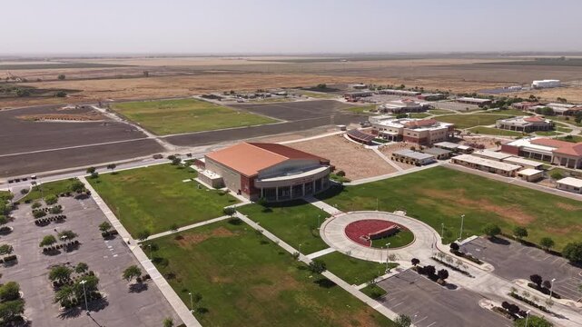 Panning aerial view showing the modern campus of West Hills College in Lemoore, California, with its green lawns, academic buildings, large theater, and expansive parking lots on a clear day