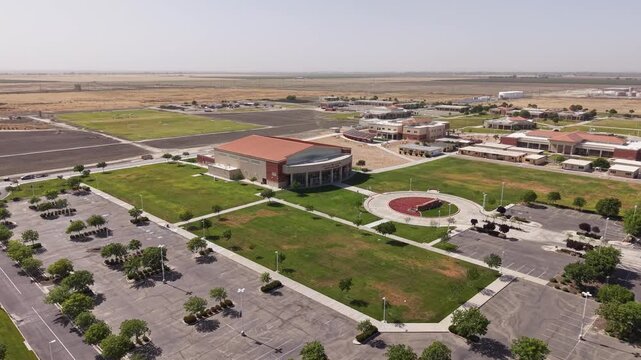 Descending drone view of the West Hills College campus in Lemoore, California, showcasing the modern architecture, empty parking lots, green spaces, and surrounding agricultural landscape