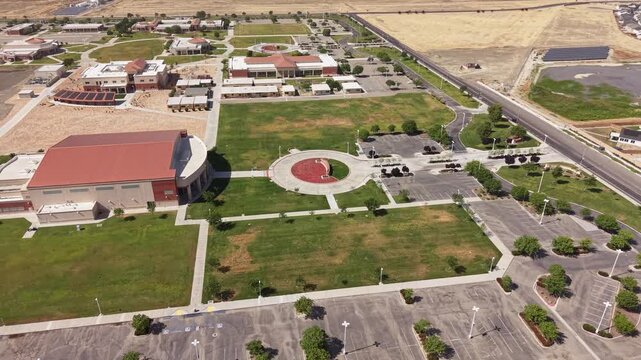 Ascending drone footage flying over the Lemoore College campus, showing the modern university buildings, green lawns, and large, empty parking lots on a sunny day in Central California
