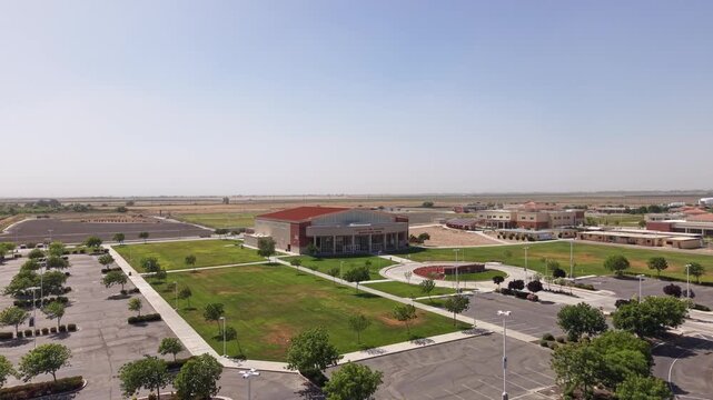Aerial drone footage rising above the West Hills College campus in Lemoore. California. Revealing the buildings. Empty parking lots. Green lawns. And surrounding agricultural landscape on a clear day