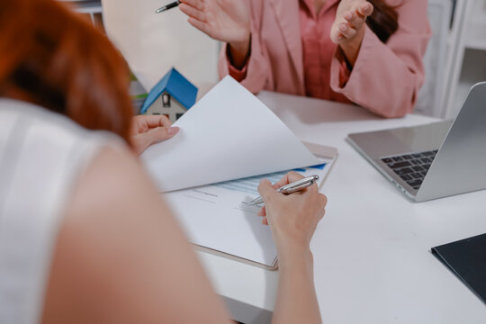 Real estate agent reviewing property documents and insurance paperwork with a client before handing over house keys, representing a successful home purchase and ownership transfer.