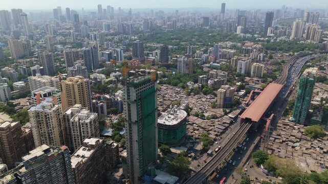 Stunning aerial view of mumbai showing contrast between rising skyscrapers and high rises beside sprawling dense slums and a busy train station, highlighting stark urban inequality