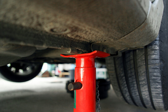 Closeup of red jack stand supporting the underbody frame of a lifted car during auto repair or maintenance work