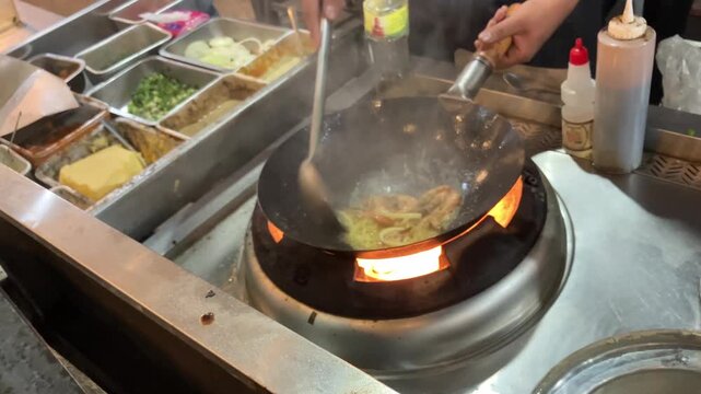 4K handheld static close up of a professional chef cooking fresh shrimp inside a hot wok with open fire stove Stir frying seafood at commercial kitchen or street food stall broll for culinary