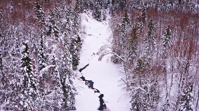 Drone view of a calm winter scene with a river bordered by snow-covered surroundings.