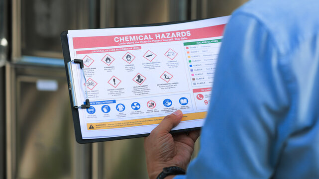 Focused inspector holding clipboard ensures chemical storage compliance during outdoor industrial safety audit with serious attention