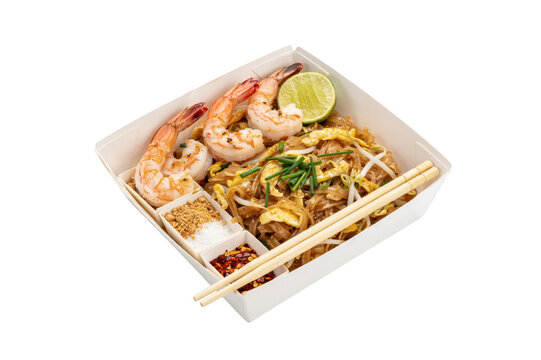 Takeaway box of thai pad thai noodles with large grilled shrimp, lime wedge, bean sprouts, and side condiments, isolated on black background