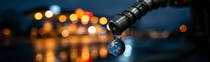 Fototapeta premium Earth in a Droplet: A single droplet hanging from a gas pump nozzle reflects the Earth, symbolizing the global impact of fuel consumption, set against a blurred backdrop of city lights at dusk.