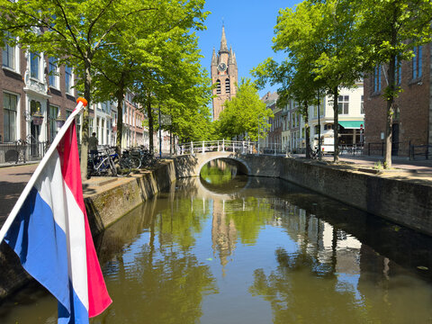 Oude Kerk Old Church leaning tower above leafy Delft canal reflections on a sunny spring day, Netherlands