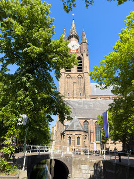 Leaning old church Oude Kerk Gothic tower above canal bridge on sunny day in Delft City Centre, Netherlands