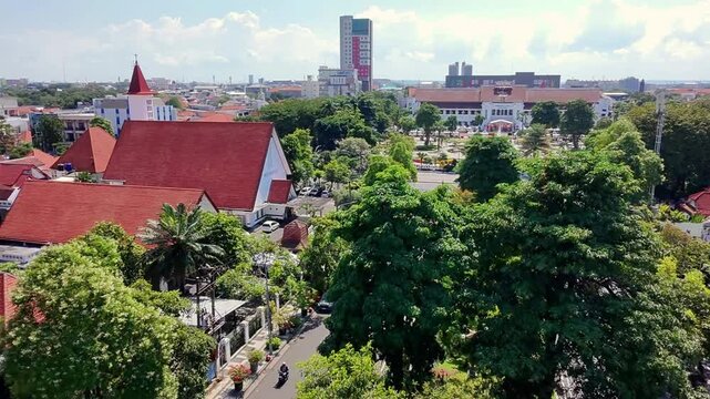 Aerial view of Surabaya cityscape with lush greenery and modern buildings on a sunny day during the Surabaya Fashion Festival in Indonesia.