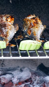 Vertical panoramic close-up video of cooking mackerel fish with vegetables on a grill barbecue