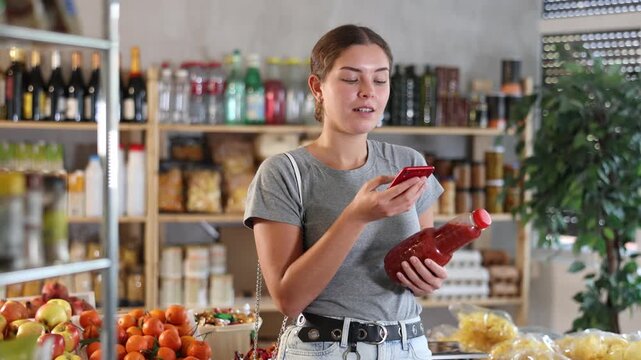 Young woman uses her phone to scan tomato juice, read the composition and calorie content of the drink. Customer in a supermarket scans the qr code of the juice and pays through the banking app. High