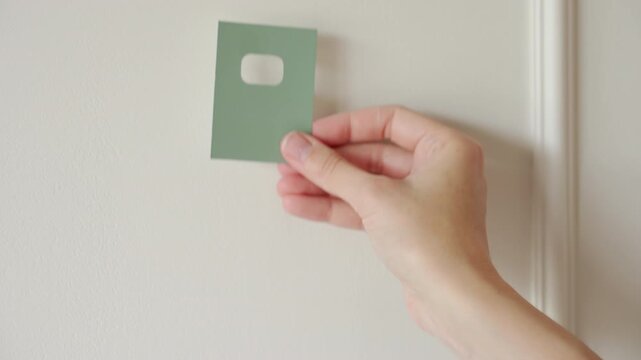 Hands choosing paint colors for wall holding green paint samples near a light wall. Concept of home renovation wall painting and interior design.
