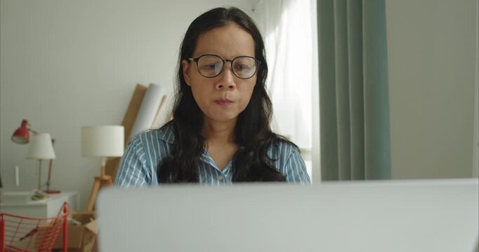Asian middle female wear glasses typing working on computer, Asia business woman using  laptop at home office, Front view