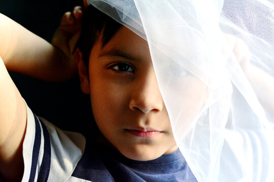 Calm boy hiding part of the face with translucent textile.