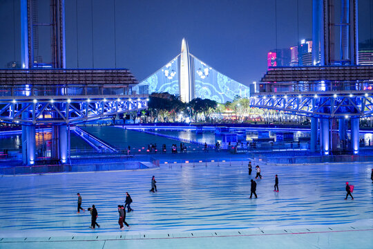 Guangzhou, Guangdong Province, China - 24 February 2024: View of the illuminated Haixinsha Asian Games Park at night with people walking across the blue-lit plaza.