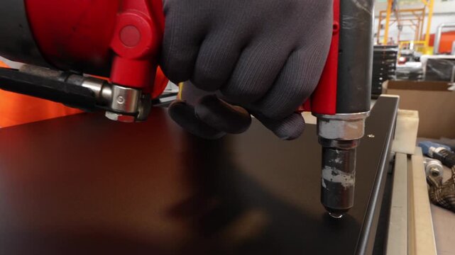 Gloved worker operating fastening tool on sheet metal in factory