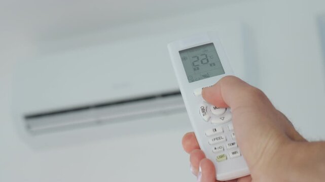 Hand using remote control to change the temperature on air conditioner . Concept of cooling summer heat