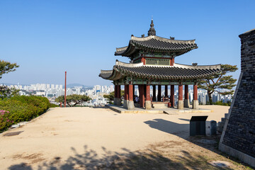 Fototapeta premium Traditional Seojangdae pavilion at Hwaseong Fortress with modern Suwon city skyline in the background.