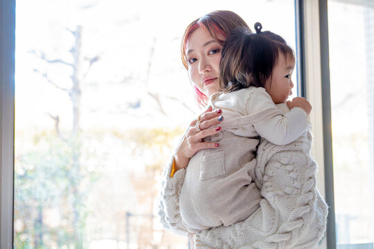 Candid portrait of an Asian mother holding her toddler and looking directly at the camera over her shoulder