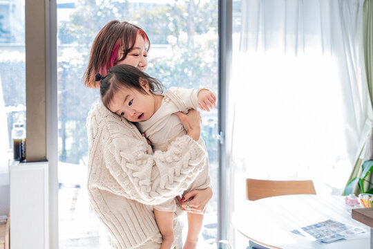 Loving Asian mother holding her sweet toddler affectionately in a bright sunlit room
