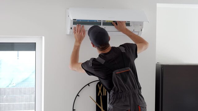 Man servicing an open wall air conditioner checking the filter panel. Concept of AC repair maintenance and cooling system service.